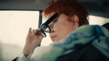 a woman with red hair is wearing glasses while sitting in a car