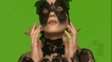 a woman wearing a black mask and a black lace top is covering her face with her hands on a green screen .