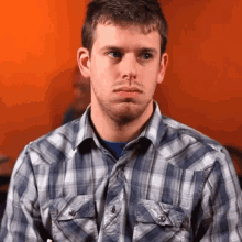 a man in a plaid shirt looks at the camera with a serious look on his face