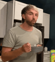 a man with a beard is eating cereal from a bowl in a kitchen
