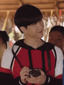 a young man in a red white and black sweater holds a camera