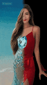 a woman in a red dress with a diamond on her chest stands on a beach