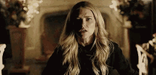 a woman with long blonde hair is standing in a dark room with a fireplace in the background .