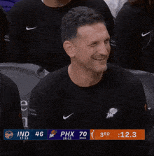 a man in a black nike shirt is smiling in front of a scoreboard that says phx 70