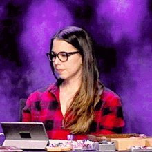 a woman wearing glasses is sitting at a table with a tablet