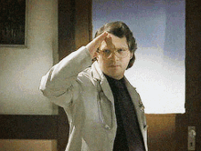 a man wearing glasses and a white jacket salutes while standing in front of a door
