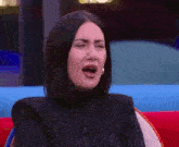 a woman in a black jacket is sitting on a red couch and making a face .
