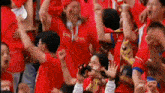 a crowd of people wearing red shirts are watching a soccer game .