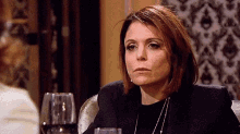a woman is sitting at a table with glasses of wine and making a funny face .