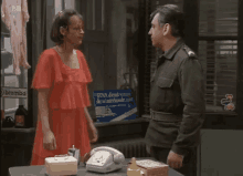 a woman in a red dress talking to a man in a military uniform in front of a brembo sign