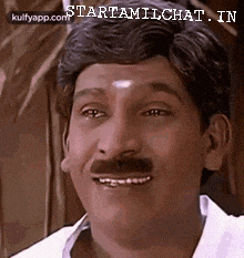 a man with a mustache and a white shirt is smiling and looking at the camera .