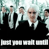 a man in a suit and tie is standing in front of a group of people with the words `` just you wait until '' below him .
