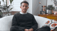 a man in a black sweater sits on a white couch in front of a table with the year 1988 on it