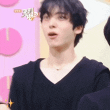 a man in a black shirt is making a funny face in front of a pink wall .