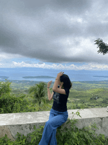 a woman sitting on a wall taking a picture of a body of water