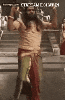 a man with long hair and a beard is dancing in front of a group of people .