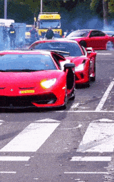 a row of red sports cars are driving down a street with a yellow truck behind them that says ' logistics ' on it
