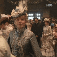 a woman wearing a feathered hat is standing in front of a crowd with hbo written on the bottom