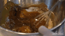 a person is whisking a mixture in a metal bowl with the words made in animatica on the bottom .