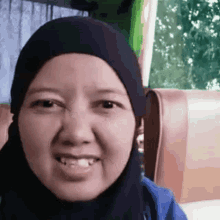 a woman wearing a black hijab and a blue jacket smiles for the camera