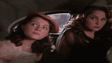 three women are sitting in a car and one of them is wearing a hat