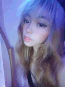 a girl with long blonde hair is taking a selfie with a blue light behind her