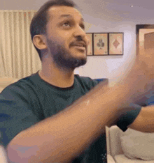 a man with a beard is sitting on a couch in a living room with his arms outstretched .
