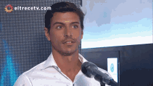 a man in a white shirt stands in front of a microphone with eltrecetv.com in the background