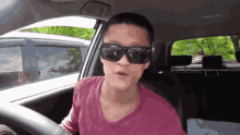 a man wearing sunglasses is driving a car .
