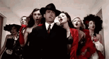 a man in a suit and tie is surrounded by a group of women in red dresses .