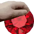 a close up of a hand holding a large red diamond