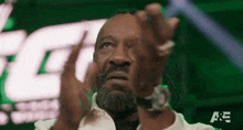 a man with dreadlocks and a beard is clapping his hands in front of a green screen .