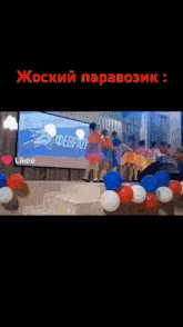 a group of young girls are dancing on a stage with balloons and a projector screen behind them