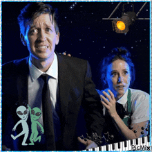 a man in a suit and tie stands next to a woman in a green apron with aliens on it