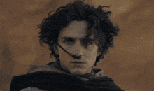 a man with curly hair and blue eyes wears a black nose clip