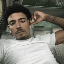 a man in a white shirt is sitting in the back seat of a car with his hand on his face