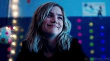 a woman with blonde hair is smiling in front of a wall with christmas lights hanging from it .