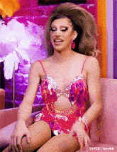 a drag queen is sitting on a pink couch wearing a pink dress .