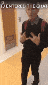 a man with a backpack is standing in a hallway with the words tj entered the chat above him .