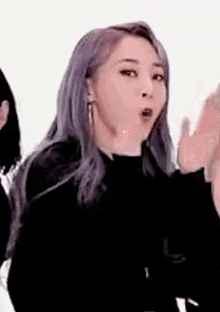 a woman with purple hair is wearing a black shirt and earrings .