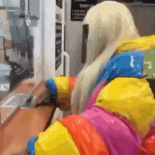 a woman in a colorful jacket sits at a counter in front of a sign that says ticket