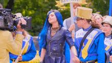 a woman with blue hair is being filmed by a cameraman while standing next to a band .