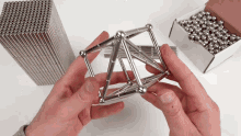 a person is holding a metal structure in their hands in front of a box of metal balls