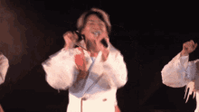 a man singing into a microphone in a dark room with other people