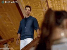 a man in a blue shirt and white pants is standing on a set of stairs looking at a woman .