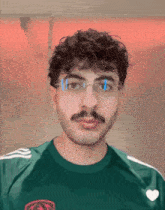 a man with glasses and a mustache is wearing a green shirt with a heart on it