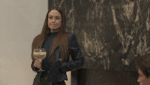 a woman in a leather jacket holds a glass of liquid