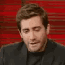 a man in a suit is making a funny face while sitting in front of a red wall .