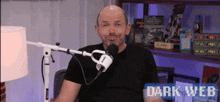a man in a black shirt is sitting in front of a microphone with dark web written on the screen behind him