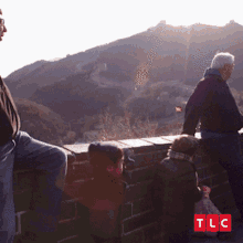 a group of people standing on a wall with tlc written on the bottom right
